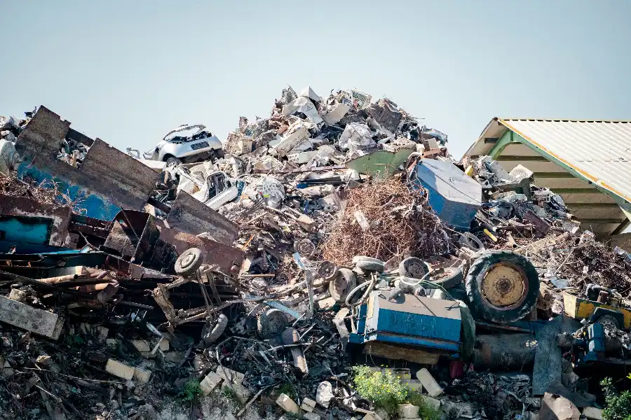 Large pile of mixed scrap metal including a car body, tyres, appliances and rusty steel stacked in a scrapyard