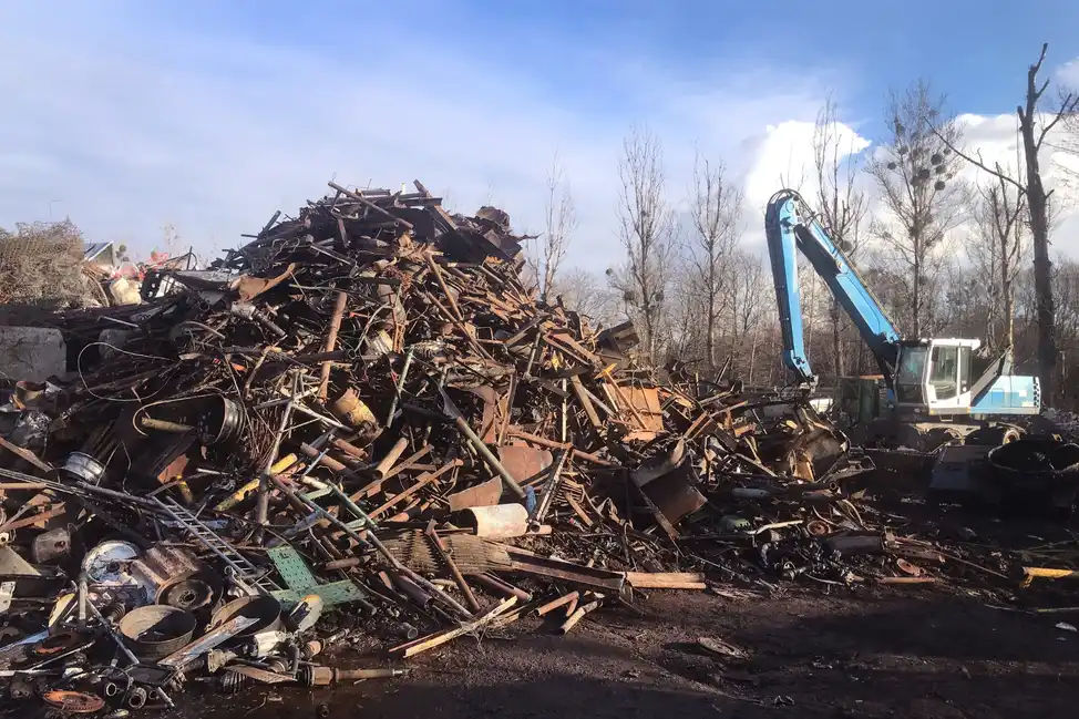 Heavy machinery beside a massive heap of mixed scrap metal under a cloudy sky.