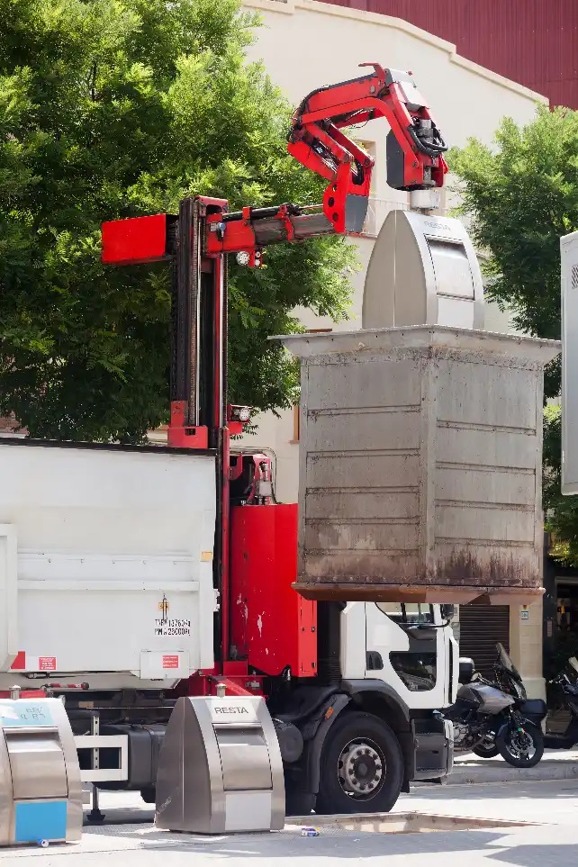 Waste collection truck using a crane arm to lift a large street waste container