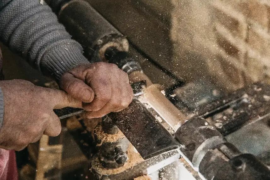 Close-up of a woodworker shaping a piece of wood on a lathe, with wood shavings flying